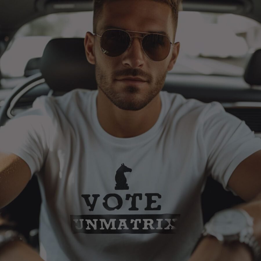 Man wearing sunglasses and a white t-shirt with "Breaking Free" printed on it, sitting in a car.