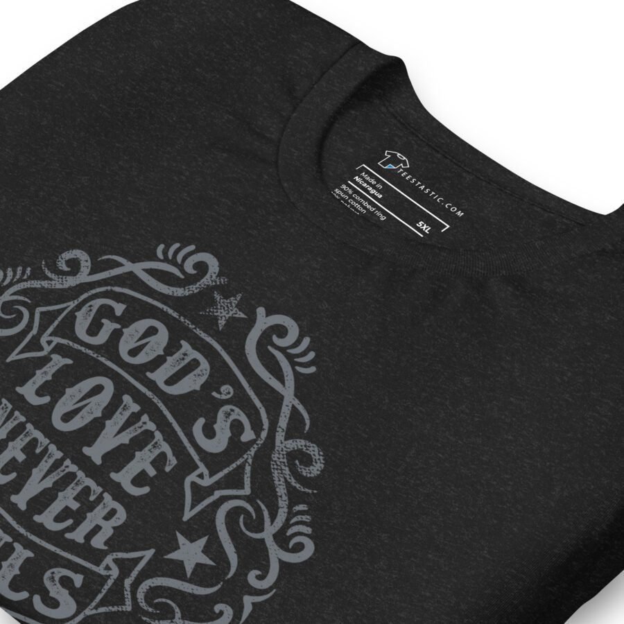 Close-up of a black unisex t-shirt with the phrase "God's Love Never Fails" written in ornate lettering. The label indicates the brand "Lazy Jacks" and size "S/CL.