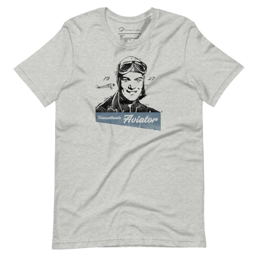 The Transatlantic Aviator unisex T-shirt in light gray features a vintage-style illustration of an aviator wearing goggles and a helmet, with the text "Transatlantic Aviator" prominently displayed along with the year "1927.